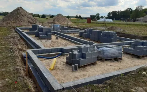 Budowa fundamentów z bloczków betonowych. Zastanawiasz się, ile kosztuje wylanie fundamentu? Na placu budowy widać materiały i postęp prac.