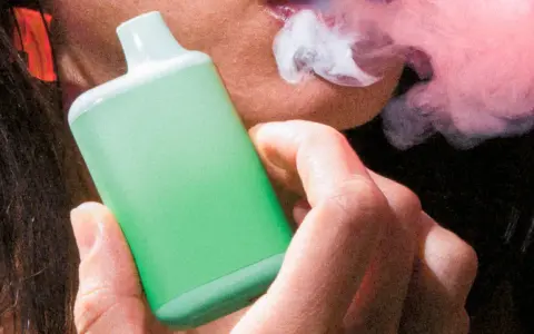 Persona vapeando un dispositivo verde, exhalando vapor. Una imagen que ilustra la diferencia entre vapear y fumar.