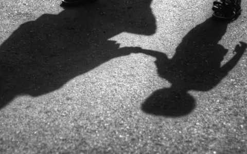 Dwie postacie, dorosła i dziecko, trzymają się za ręce. Cienie na asfalcie sugerują, że to może być dowód na reinkarnację, gdzie dusze odnajdują się w kolejnych wcieleniach.