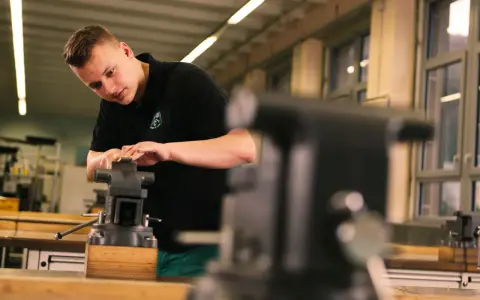 Ein junger Mann macht ein Praktikum und arbeitet konzentriert an einem Schraubstock in einer Werkstatt.