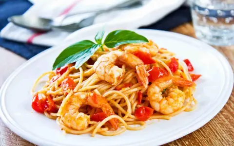 Spaghetti con gamberetti succulenti, pomodorini freschi e basilico, un piatto invitante pronto per essere gustato.