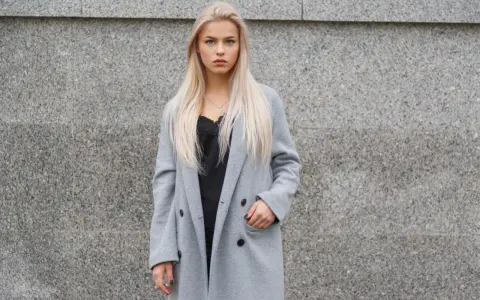 Blondynka w szarym płaszczu i czarnej koronkowej bluzce. Czerń to klasyczny wybór, jaki kolor pasuje do szarego ubrania, dodając elegancji.
