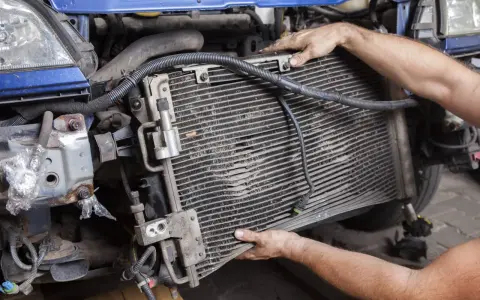 Mechanic removing a car's AC condenser, which blows hot air, for repair.