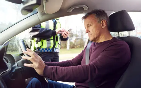 Mann am Steuer, Polizist mit Handy. Die Szene deutet auf eine Kontrolle hin, vielleicht wegen Verdacht auf **Probezeit Alkohol**.