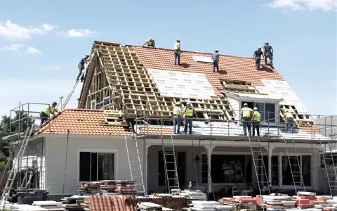 Ekipa budowlana w kaskach remontuje dach domu, używając drabin i rusztowań.