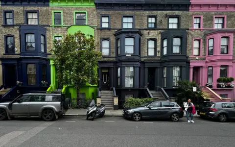 Fila de casas de colores vibrantes en Londres, con fachadas azules, verdes y rosas, estacionadas junto a coches y una moto.