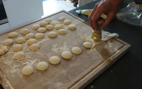 Ręcznie robione ciasto na ravioli, wycinane okrągłym wykrawaczem. Widać wiele gotowych krążków na desce.
