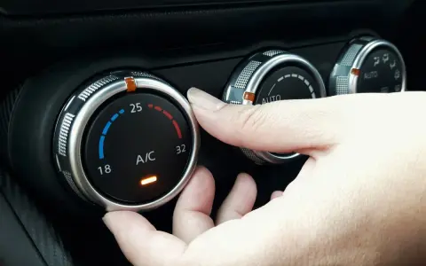 Dłoń reguluje pokrętłem temperaturę klimatyzacji w samochodzie, ustawiając ją na 25 stopni.