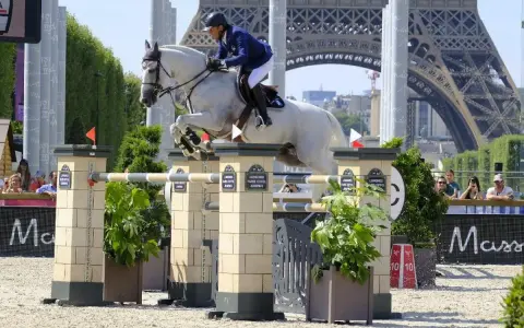 Un cavalier et son cheval blanc, Rahotep de Toscane, franchissent un obstacle à Paris, avec la Tour Eiffel en arrière-plan.