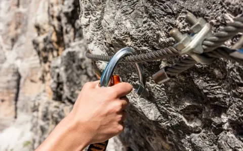 Dłoń zapina karabinek do stalowej liny na via ferrata. Bezpieczeństwo podczas wspinaczki.
