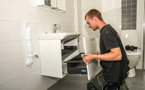 En rörmokare utför vvs arbeten i ett badrum, monterar ett nytt handfat och skåp.