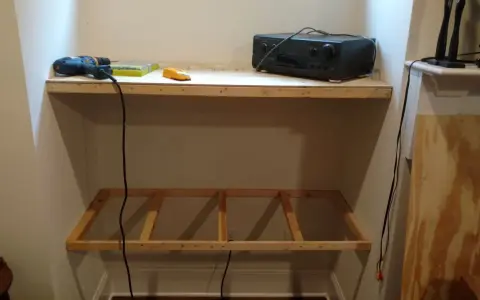 DIY project: a drill, screws, and audio receiver are on a shelf, with a wooden frame below, ready for how to hang shelves.