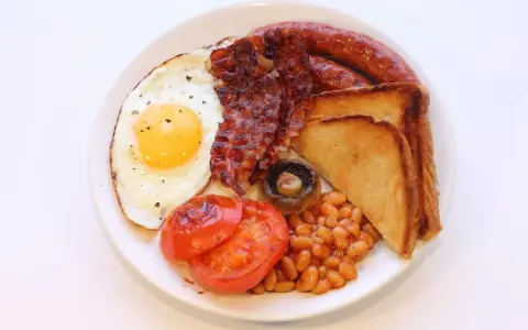 Un piatto tipico inglese con uovo fritto, bacon croccante, salsiccia, fagioli stufati, pomodori grigliati, fungo e toast.