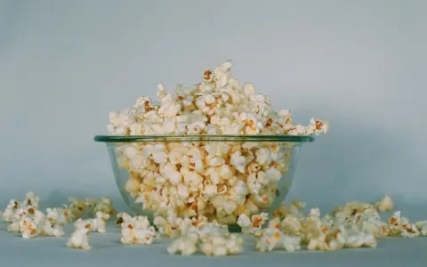 Góra popcornu w szklanej misce, rozsypane ziarna wokół. Ile popcorn kcal?