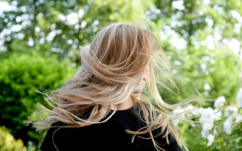 Warkocze wiatru rozwiewają chłodny blond włosów dziewczynki na tle zieleni.