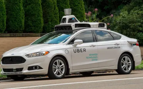 Ein weißes Uber auto mit Sensoren auf dem Dach fährt auf einer Straße.