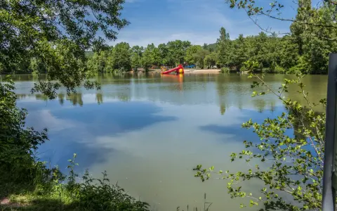 Idyllischer sulzfeld badesee mit Spielplatz und Rutsche, umgeben von grünen Bäumen.