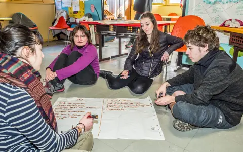 Quatre jeunes discutent autour d'un papier, participant à un mouvement d'éducation populaire. Ils brainstorment des idées pour améliorer une activité.