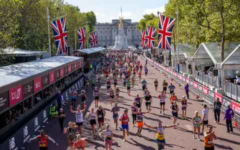 Tysiące biegaczy na trasie maratonu londyn, z flagami Wielkiej Brytanii i Pałacem Buckingham w tle.