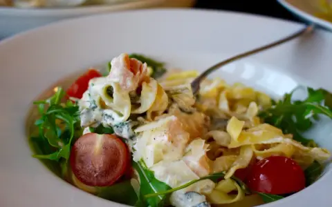 En krämig laxpasta med spenat, körsbärstomater och ruccola. En gaffel lyfter upp en bit av den läckra pastan.