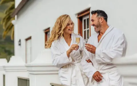Para relaksu w hotelach spa w Polsce. Uśmiechnięta para w szlafrokach wznosi toasty szampanem na balkonie.