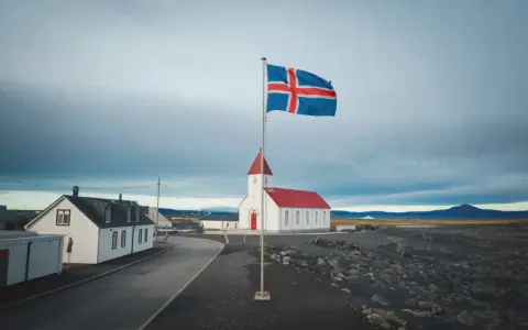 Islandia praca: biały kościół z czerwoną wieżą i flagą Islandii na tle pochmurnego nieba.