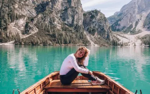 Kobieta w łodzi na turkusowym jeziorze w Dolomitach, w tle góry i las.