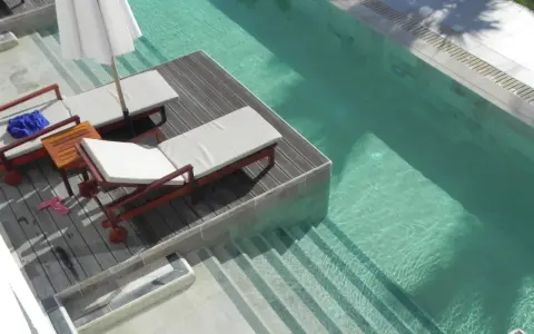 Tumbonas y sombrilla junto a unas piscinas originales de agua cristalina con escalones integrados.