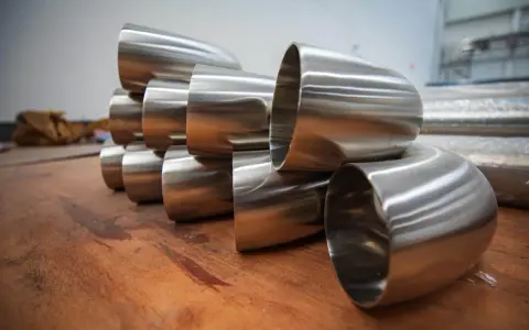 Pièces métalliques brillantes, probablement des coudes pour un poêle à bois conduit, empilées sur une surface en bois.
