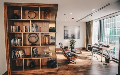 Drewniana biblioteczka z książkami i dekoracjami, obok skórzane fotele i biurko z maszyną do pisania. Styl **modern rustic**.