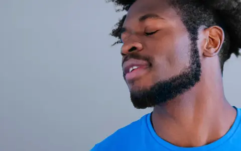Hombre con barba cortina y cabello afro, ojos cerrados, con expresión de paz.