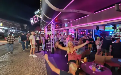 Nachts auf der Albufeira Partymeile: Menschen tanzen und feiern unter Neonlicht in Bars und Clubs.
