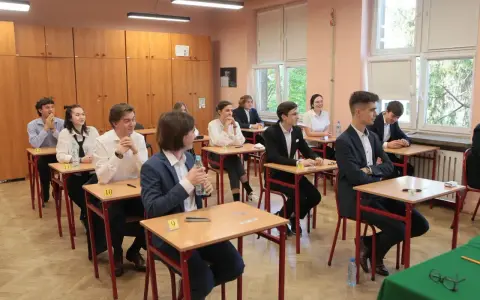Uczniowie siedzą w ławkach podczas egzaminu. Zastanawiają się, ile trwa matura z biologii, skupieni na zadaniach.