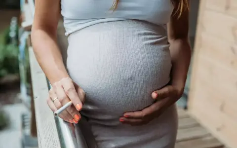 Schwanger, rauchen und stillen sind keine gute Kombination. Eine Frau hält eine Zigarette in der Hand, während sie ihren Bauch streichelt.
