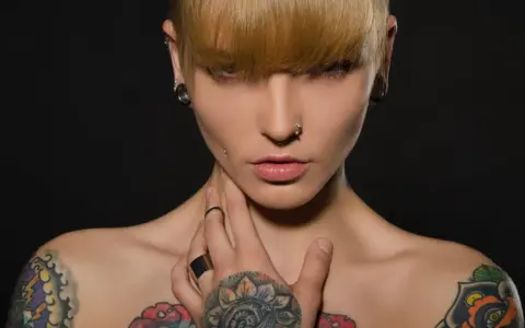 Kobieta z tatuażami na klatce piersiowej i ramionach, kolczykami w uszach i nosie. Czy tatuaże są szkodliwe?