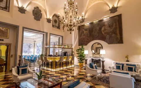 Elegant hotel lounge with a bar, fireplace, ornate chandelier, and artwork.