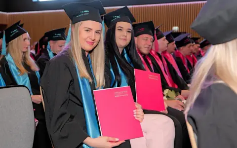 Absolwentki w togach i biretach Akademii WSB, z dyplomami w rękach, świętują zakończenie studiów na kierunku filologia angielska.