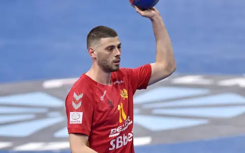 Branko Vujović, zawodnik piłki ręcznej, w czerwonej koszulce z numerem 11, trzyma piłkę nad głową.