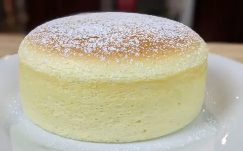 Un délicieux cheesecake japonais, léger et aérien, saupoudré de sucre glace sur une assiette blanche.