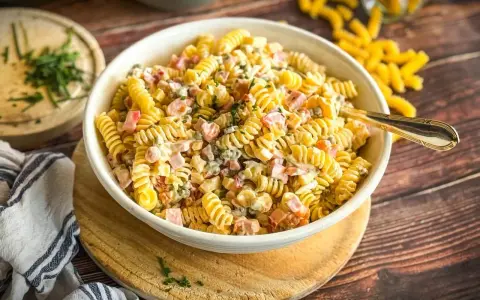 Cremiger Nudelsalat mit Schinken, Erbsen und einem leckeren Dressing, garniert mit frischen Kräutern.