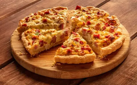 Fette di torta salata patate e salsiccia dorata e invitante, servite su un tagliere di legno.