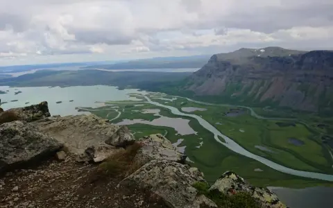 Vacker utsikt över Rapadalen med Skierfe i bakgrunden. En slingrande flod flyter genom ett grönt landskap med sjöar.