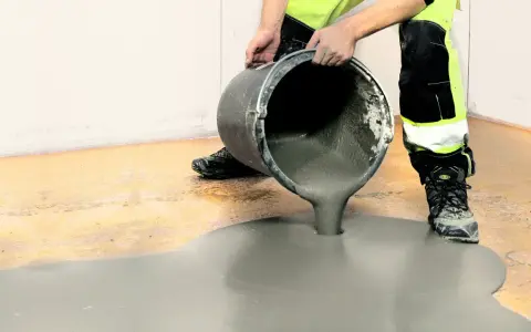 Person i varselkläder häller flytspackel på ett garagegolv för att jämna ut det.