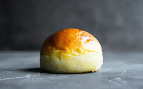 Ein goldbraunes Brioche-Brötchen liegt auf einer dunklen Oberfläche.