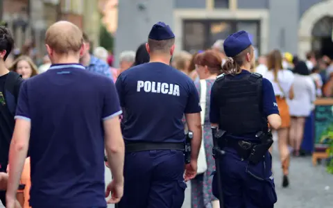 Policja w patrolu, kiedy policja szuka dłużnika. Dwóch funkcjonariuszy w mundurach idzie ulicą wśród tłumu ludzi.