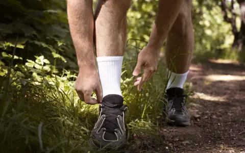 Biegacz przygotowuje się do treningu, sznurując buty. Dobre **jakie skarpetki do biegania** to podstawa komfortu na leśnej ścieżce.