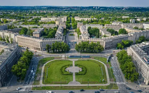 Plac Centralny w Nowej Hucie z socrealistyczną zabudową, zielonymi skwerami i torami tramwajowymi.