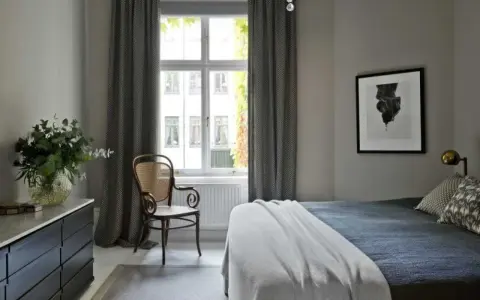 Sovrum med en säng, en stol och en byrå. Konst av Sofia Wallenstam på väggen.