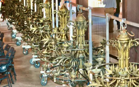 Une rangée de grands candélabres dorés, prêts pour un événement. Ce lustrier métier, complexe et orné, attend d'illuminer la scène.