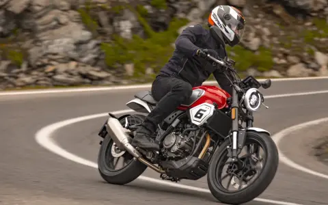 Motocyklista w kasku jedzie czerwonym motocyklem po krętej drodze. Idealny motocykl na początek przygody z jazdą.
